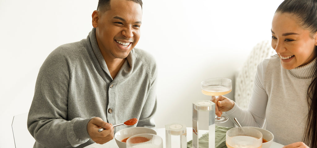 A man and woman laughing and eating soup at a table.